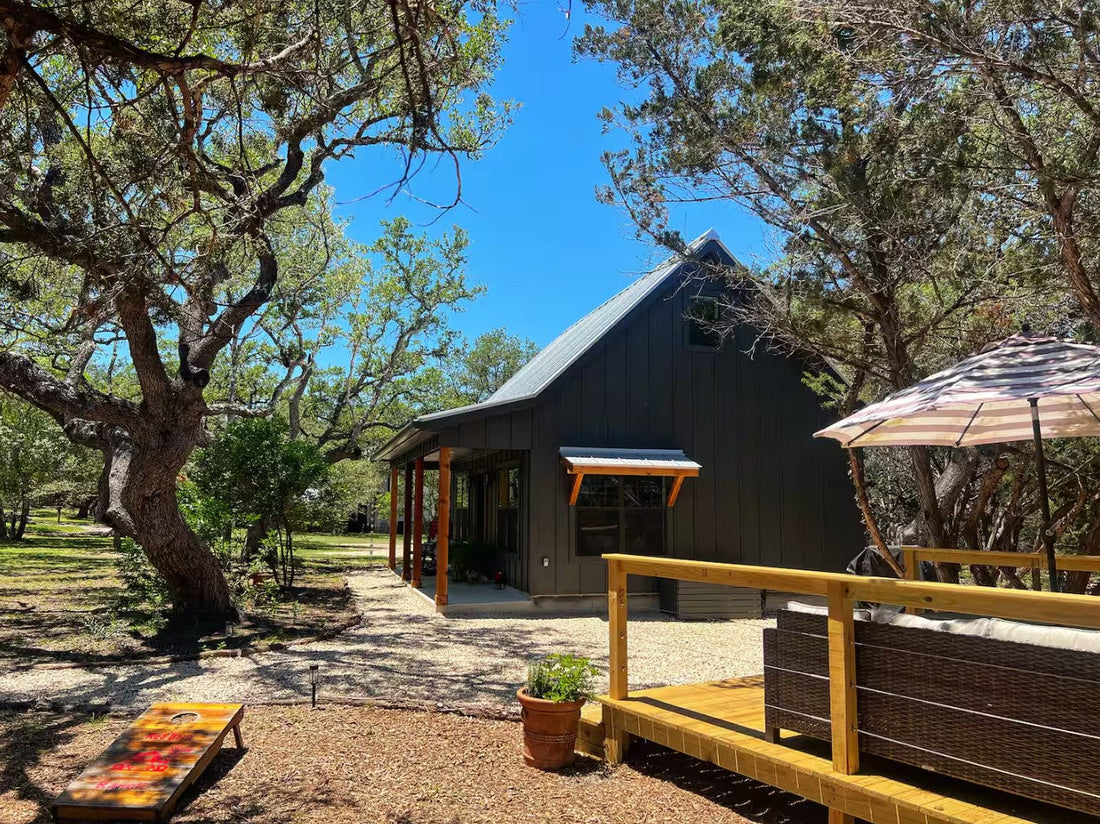 a black and wood exterior small cabin built on a flat land with mature trees and concrete patio.