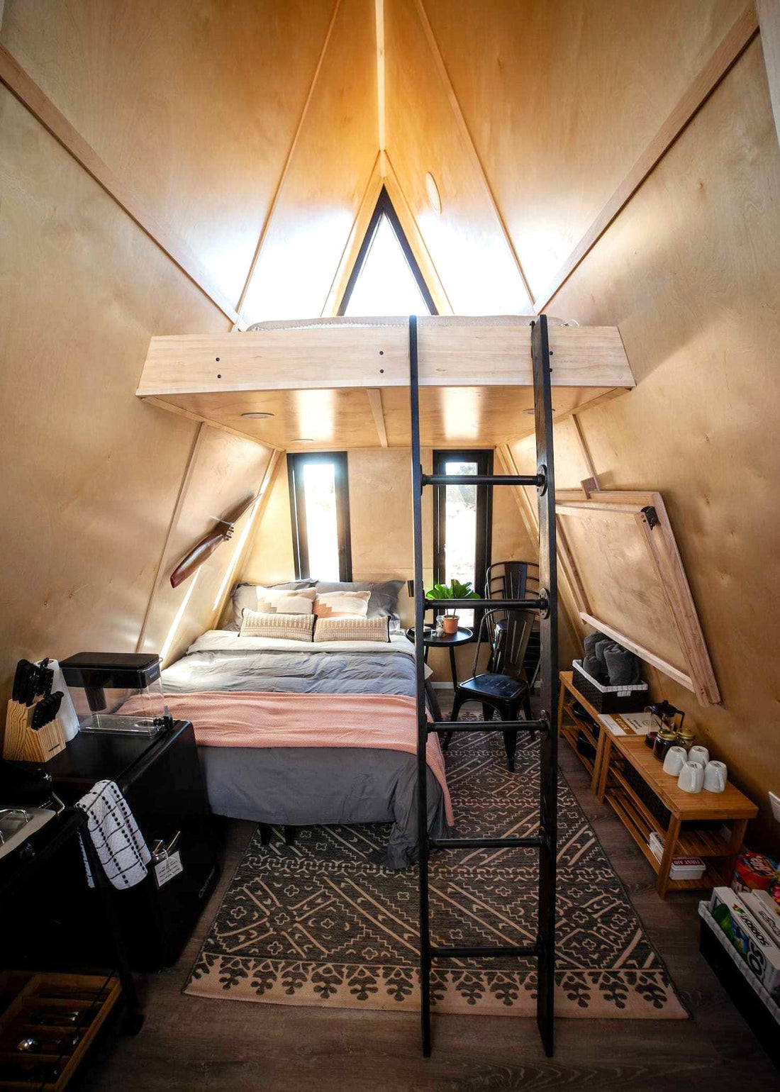 Interior photo of a small A-frame cabin with full size bed and a loft. 