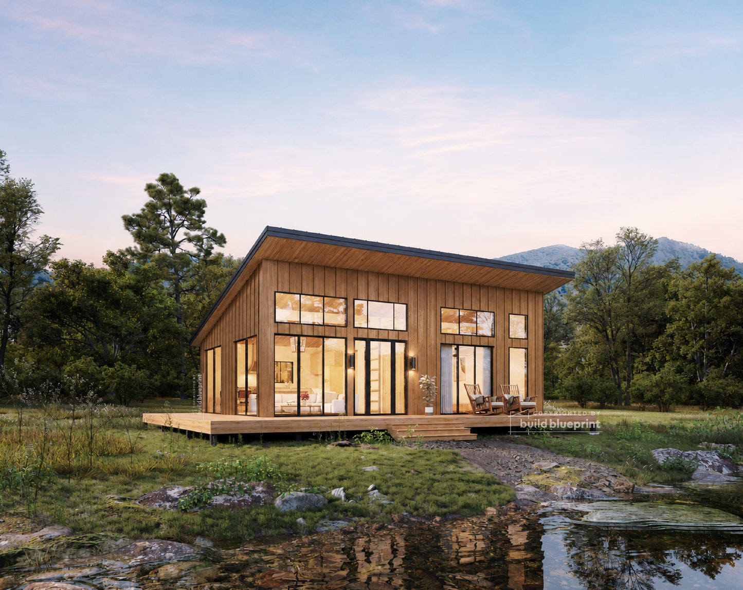 A modern single-story wooden cabin with large floor-to-ceiling windows, a dark roof, and a wooden deck, situated in a grassy outdoor setting with trees, mountains, and a small stream in the foreground.