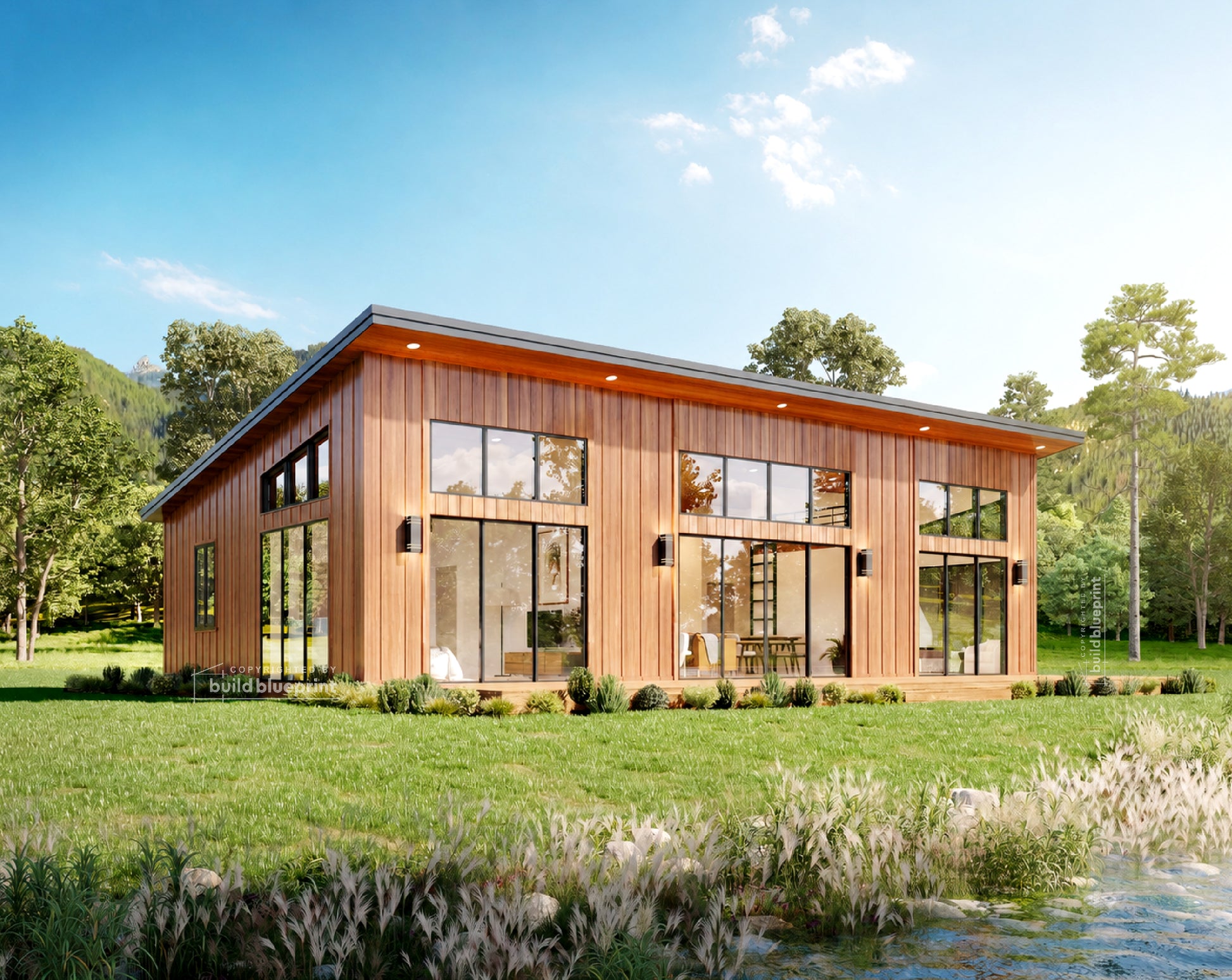 Modern single-story house with dark gray vertical siding, large floor-to-ceiling windows, and a wooden deck, situated beside a rocky stream with trees and hills in the background.